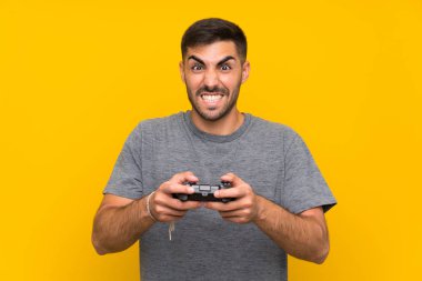 İzole sarı arka plan üzerinde bir video oyunu denetleyicisi ile oynayan genç yakışıklı adam