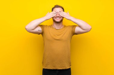 Sarışın adam izole sarı duvar eller tarafından gözleri kaplama
