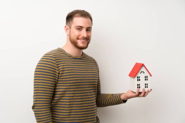 Küçük bir ev tutan izole beyaz duvar üzerinde yakışıklı adam