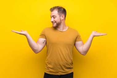 İki eliyle copyspace tutan izole sarı duvar üzerinde Blonde adam