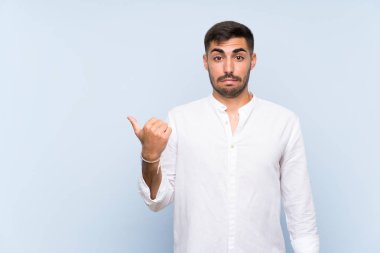 Izole mavi arka plan üzerinde sakallı yakışıklı adam mutsuz ve yan işaret