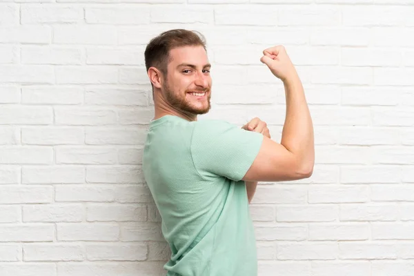 Blonde man over brick wall making strong gesture