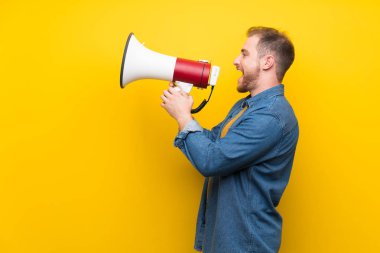 Bir megafon üzerinden bağıran izole sarı duvar üzerinde sarışın adam