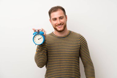 Vintage çalar saat tutan izole beyaz duvar üzerinde Yakışıklı adam