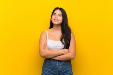 Genç genç Asyalı kız izole sarı arka plan üzerinde gülümseyerek yukarı bakıyor