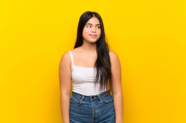 Izole sarı arka plan üzerinde genç genç asyalı kız yan görünümlü şüpheler jest yapma