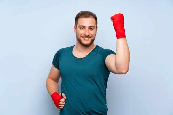 Blonde sport man over blue wall in boxing bandages