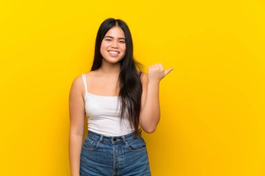 Izole sarı arka plan üzerinde genç genç Asyalı kız bir ürün sunmak için yan işaret