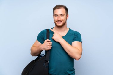 Mavi duvar üzerinde Blonde spor adam bir ürün sunmak için yan işaret