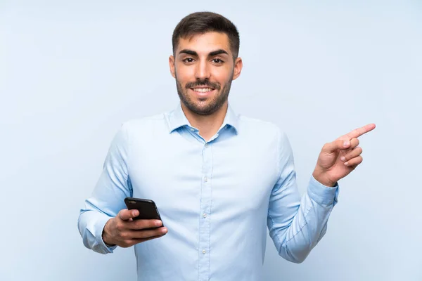 Joven Hombre Guapo Con Móvil Sobre Aislada Pared Azul Sorprendido —  Fotos de Stock