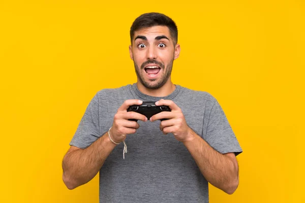 Joven hombre guapo jugando con un controlador de videojuegos sobre fondo amarillo aislado —  Fotos de Stock