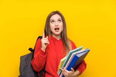 İşaret parmağı ile işaret sarı arka plan üzerinde Genç öğrenci kız harika bir fikir