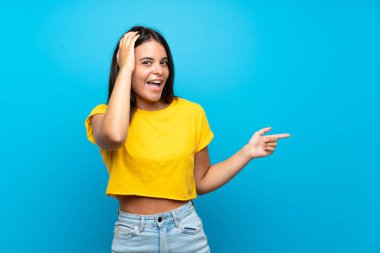 Izole mavi arka plan üzerinde Genç kız şaşırttı ve yan parmak işaret
