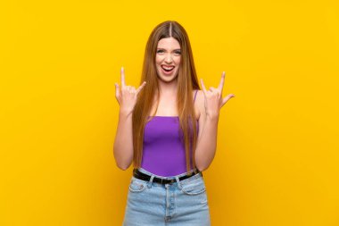 Izole sarı arka plan üzerinde rock jest yapma genç kadın