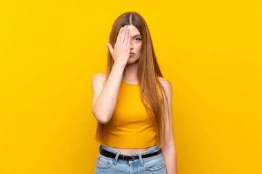 Elle bir göz kapsayan izole sarı arka plan üzerinde genç kadın