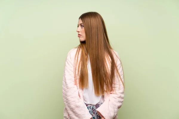 Young woman in dressing gown over green wall looking side