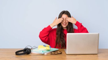 Genç öğrenci kız elleri ile gözleri kaplayan bir masada okuyan