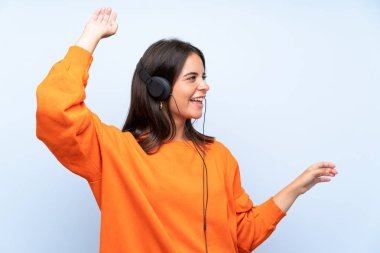 Genç kadın bir mobil ile müzik dinleme ve izole mavi duvar üzerinde dans