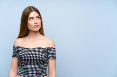 Izole mavi arka plan üzerinde genç kadın ayakta ve yan bakıyor