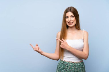 Izole mavi arka plan üzerinde genç kadın korkmuş ve yan işaret