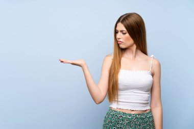 İzole edilmiş mavi arkaplan üzerinde genç bir kadın kopyalama alanını şüpheyle tutuyor