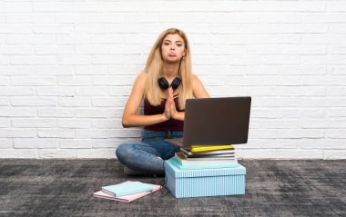 Dizüstü bilgisayarıyla yerde oturan genç kız avuç içi bir arada tutuyor. Kişi bir şey ister