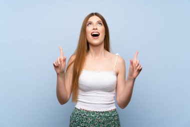 Izole mavi arka plan üzerinde genç kadın şaşırttı ve işaret