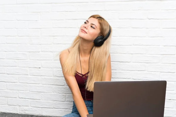 Chica adolescente sentada en el suelo con su portátil escuchando música —  Fotos de Stock