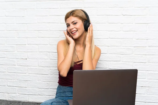 Chica adolescente sentada en el suelo con su portátil escuchando música —  Fotos de Stock