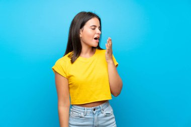 Izole mavi arka plan esneme üzerinde genç kız esneme ve el ile geniş açık ağız kapsayan