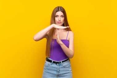 Izole sarı arka plan üzerinde genç kadın jest zaman dışarı yapma