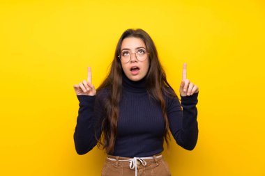 Izole sarı duvar üzerinde Genç kız şaşırttı ve işaret