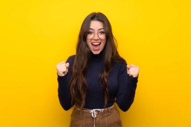 Izole sarı duvar üzerinde genç kız kazanan pozisyonda bir zafer kutluyor