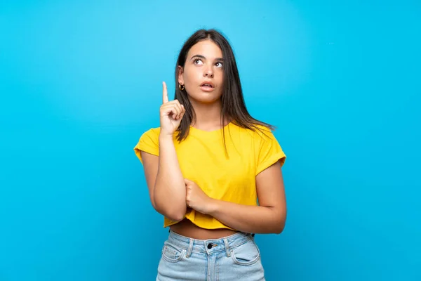 Menina Sobre Fundo Azul Isolado Pensando Uma Ideia Apontando Dedo — Fotografia de Stock