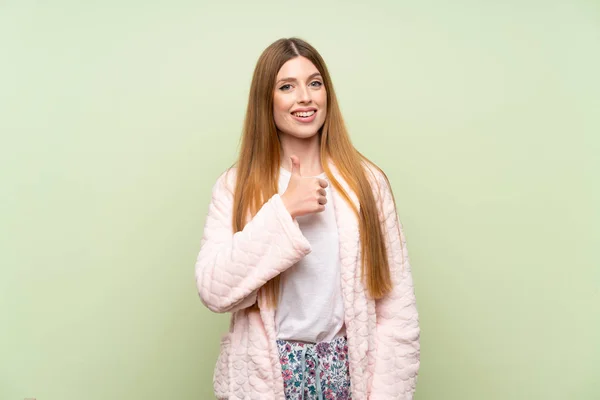 Young woman in dressing gown over green wall giving a thumbs up gesture