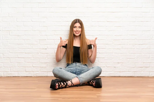 親指を上げて床に座っている若い女性 — ストック写真