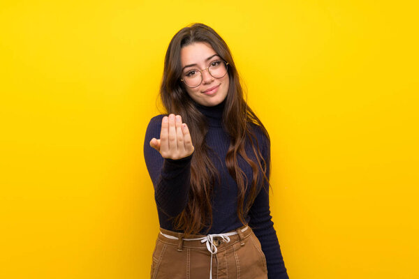 Teenager girl over isolated yellow wall inviting to come with hand. Happy that you came