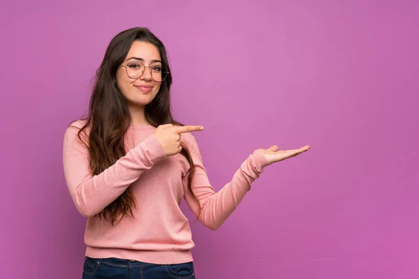 少女在紫色的墙壁上拿着模仿空间想象在手掌插入广告 — 图库照片