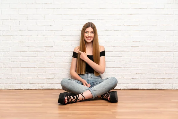 Mujer Joven Sentada Suelo Señalando Con Dedo Hacia Lado —  Fotos de Stock