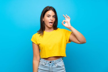 Izole mavi arka plan üzerinde Genç kız şaşırttı ve ok işareti gösteren