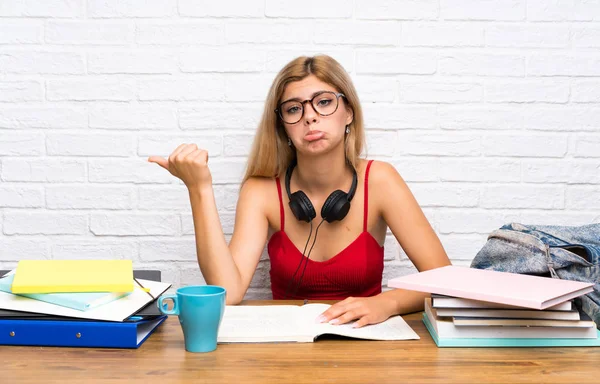 Teenager student girl at indoors unhappy and pointing to the side