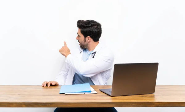 Joven Médico Con Portátil Sobre Una Pared Aislada Apuntando Hacia — Foto de Stock