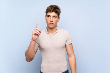Izole mavi duvar üzerinde yakışıklı genç adam bir fikir parmağını işaret düşünme