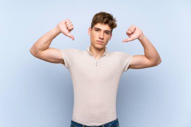 Izole mavi duvar üzerinde yakışıklı genç adam başparmak aşağı gösteren