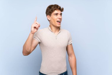 Izole mavi duvar üzerinde yakışıklı genç adam bir parmak kaldırırken çözüm gerçekleştirmek niyetinde