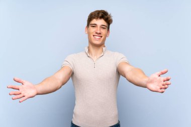 Izole mavi duvar üzerinde Yakışıklı genç adam sunan ve el ile gelmek için davet