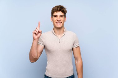 Izole mavi duvar üzerinde Yakışıklı genç adam gösteren ve en iyi işareti bir parmak kaldırma