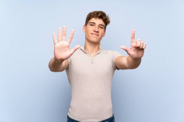 Izole mavi duvar üzerinde yakışıklı genç adam parmakları ile yedi sayma