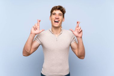 Parmakları geçerken izole mavi duvar üzerinde Yakışıklı genç adam