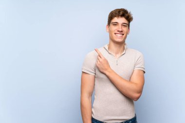 Bir ürün sunmak için yan işaret izole mavi duvar üzerinde Yakışıklı genç adam